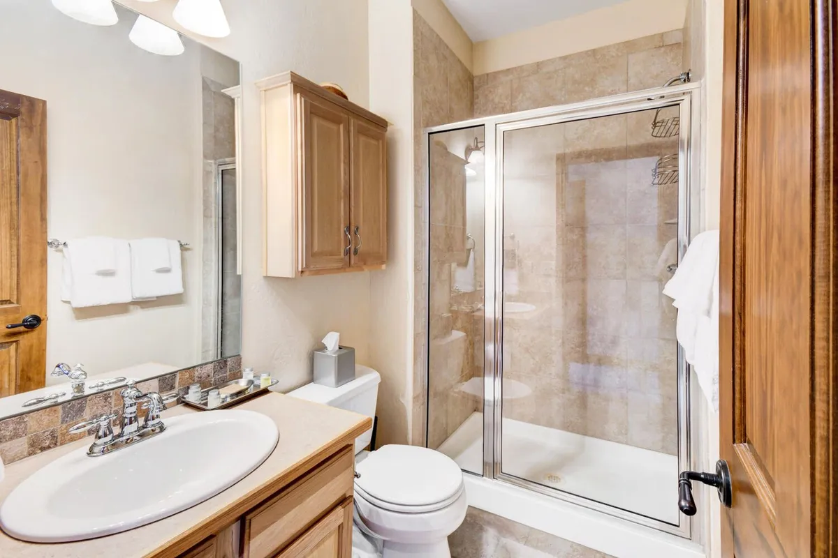A modern, spa-inspired bathroom with a glass shower enclosure, large vanity with mirror, wood cabinetry, and a clean, calming ambiance. Ample space is available for morning or evening routines.