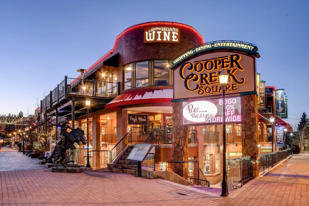 A vibrant exterior scene at Cooper Creek Square, showcasing the sign, wine shop, and an outdoor seating area. The space is lively and inviting, representing the nearby dining and entertainment options in downtown Winter Park.