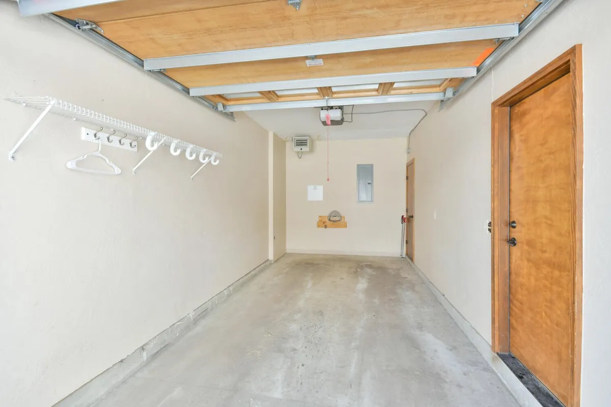 A tidy, well-lit garage with a prominent garage door, wall-mounted shelving for storage, and a wooden door for access. The space is organized for both parking vehicles and storing equipment, making it ideal for adventure gear or seasonal items.