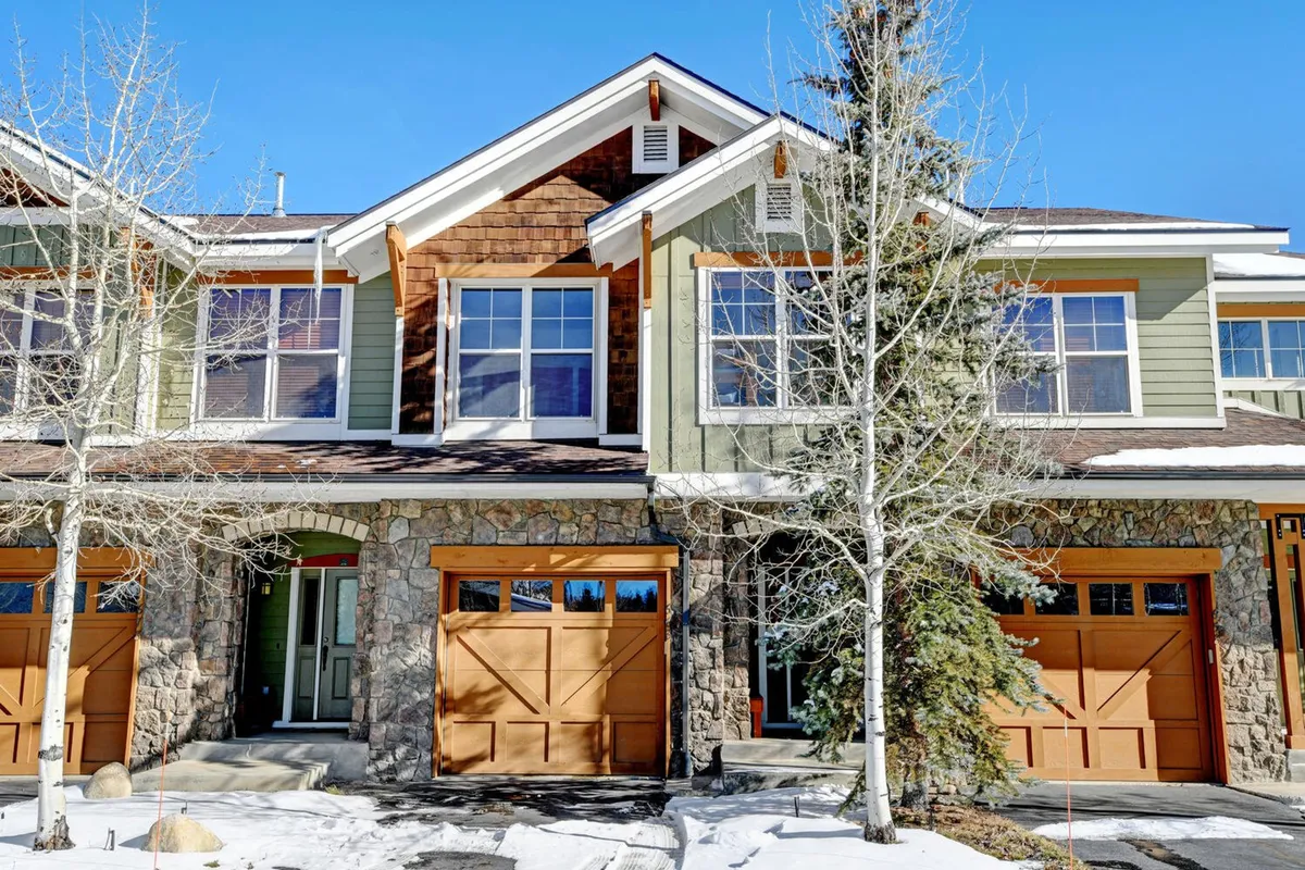 A welcoming exterior shot of the property featuring a stone facade, wooden garage doors, large windows, and a tree-lined entrance. The home sits amidst natural surroundings, inviting residents to step outside and explore the outdoors.