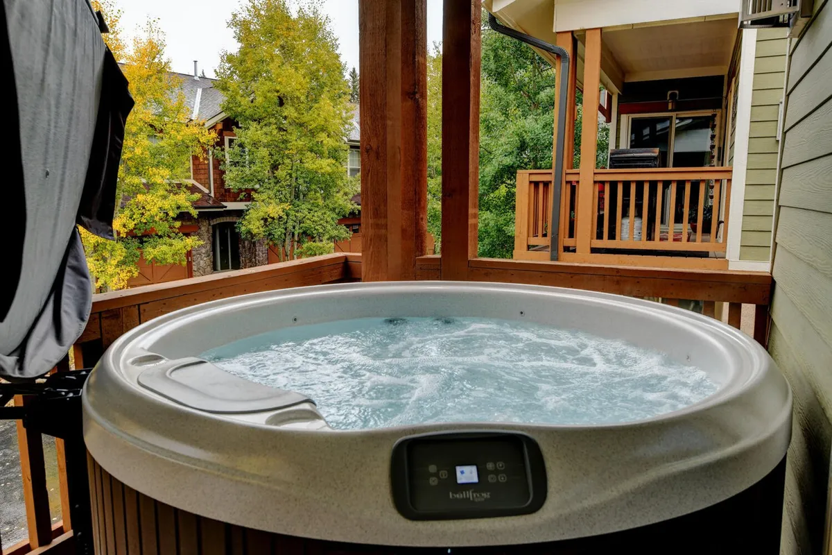 A tranquil scene with the hot tub as the centerpiece on a wooden deck, embraced by tall trees and mountain air. The layout suggests inviting moments for soaking, morning coffee, or sharing stories under the stars.