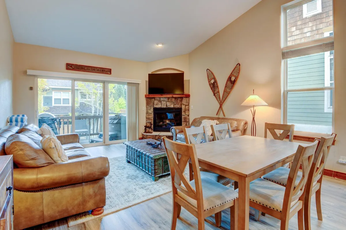 A warm, inviting living and dining space featuring a comfortable sofa, stylish fireplace, and a generous dining table set near expansive windows. The room is suffused with sunlight, radiating both coziness and elegance—ideal for gatherings and relaxation.