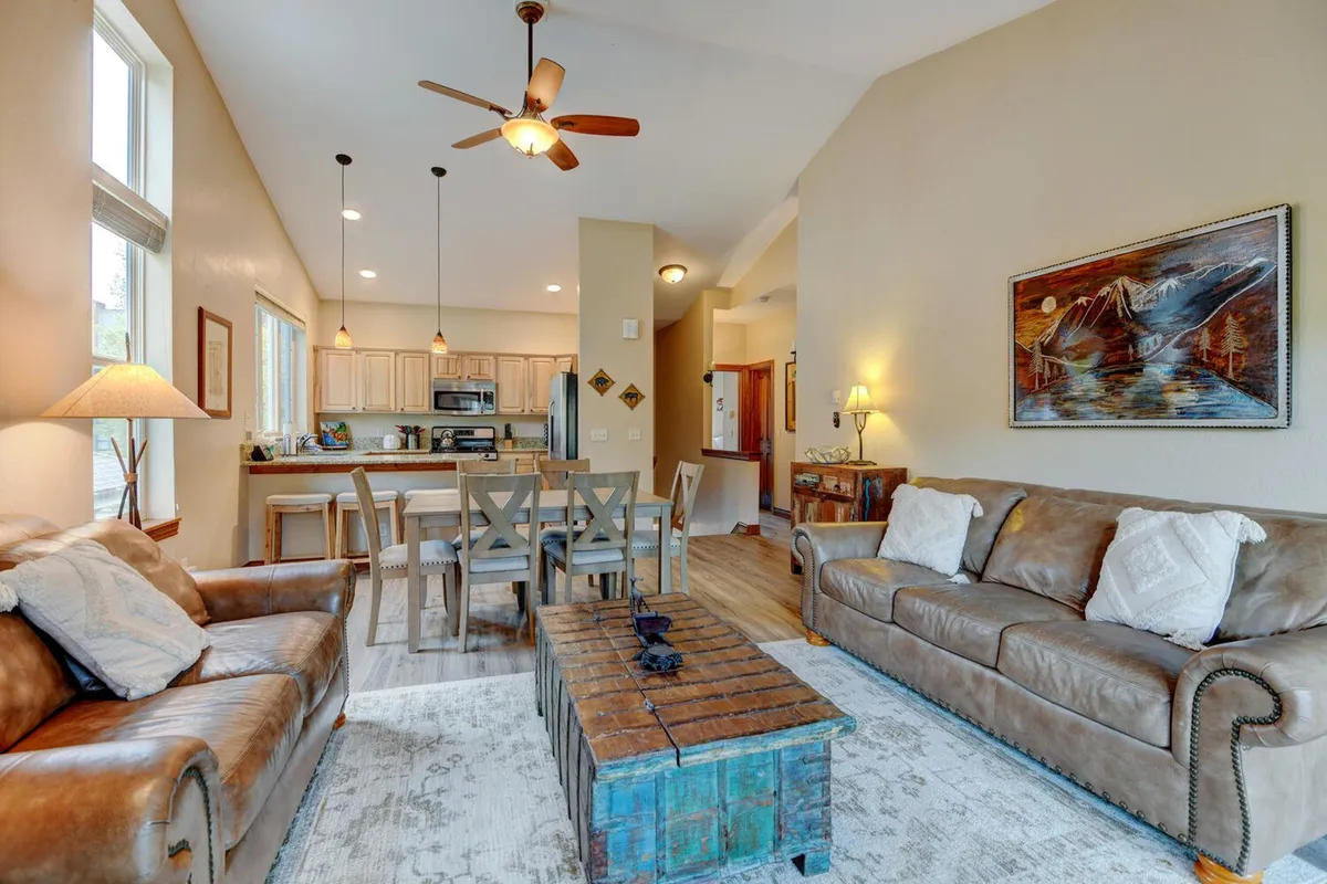 A luminous open-concept interior featuring leather sofas arranged around a wooden coffee table, with a clear view of both the dining area and the chef’s kitchen in the background. Artwork adorns the walls, and the space is bathed in natural light, emphasizing its inviting atmosphere.