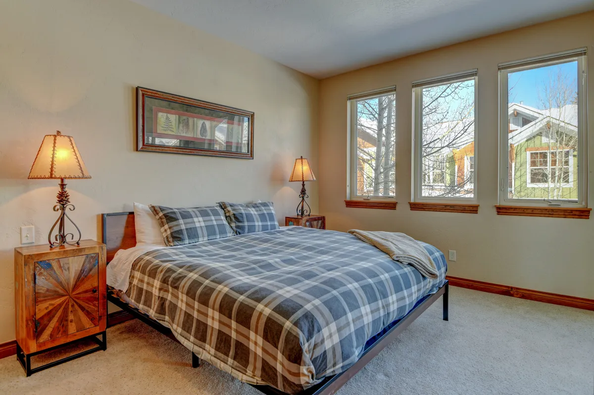 A bright, inviting bedroom featuring a comfortable bed with plush linens, bedside lamps casting soft light, and windows allowing natural daylight to stream in. The wall art adds a calming touch to the restful atmosphere.